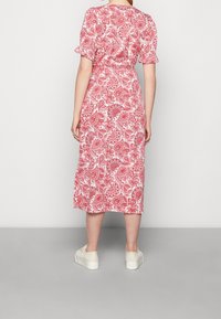 Robe midi rouge à motif cachemire avec manches courtes à volants, taille cintrée et coupe décontractée, associée à des baskets de couleur claire.