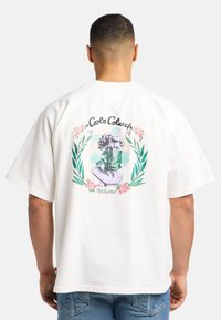 Hvid bomulds T-shirt med et stort grafisk print på ryggen, der viser en byste med en grøn maske, omkranset af blomster- og bladaffektioner.