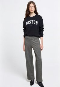 Sudadera negra con texto "BOSTON 1980", combinada con pantalones grises de pierna ancha y textura. Modelo con botines negros hasta el tobillo.