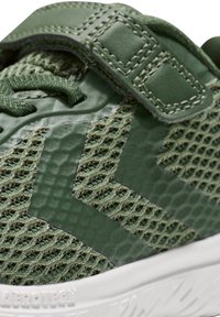 Scarpa da atletica verde con tomaia in rete caratterizzata da un motivo a spina di pesce texturizzato, dettagli in pelle e una cinghia di sicurezza in velcro. Suola in gomma bianca.