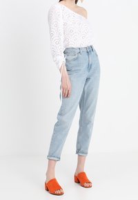 Hvid øjelet én-skulder top med bundet ærmer, lyseblå højtaljede jeans og orange ruskinds block-heel mule.