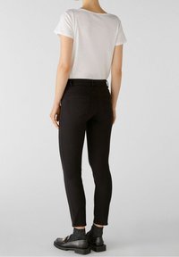 Jeans negros ajustados de tiro medio, con costuras sutiles y bolsillos traseros, combinados con una camiseta blanca de manga corta y mocasines negros.