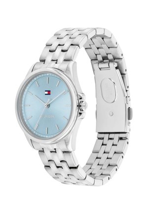 Montre-bracelet en métal argenté avec un cadran rond bleu clair, des index horaires minimalistes, trois aiguilles et un petit logo rectangulaire près de 12 heures.