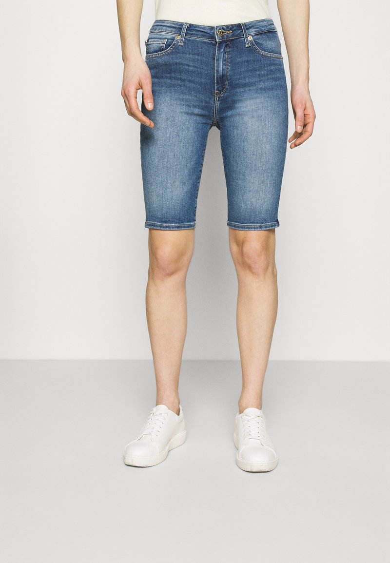 Džínové kraťasy středně modré barvy s pěti kapsami, ohrnutými lemy a zapínáním na zip, doplněné bílými teniskami.