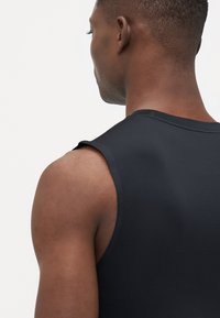 Zwart mouwloos sporttop, aansluitend ontwerp met een gladde textuur. Beschikt over smalle schoudernaad en een schone halslijn.