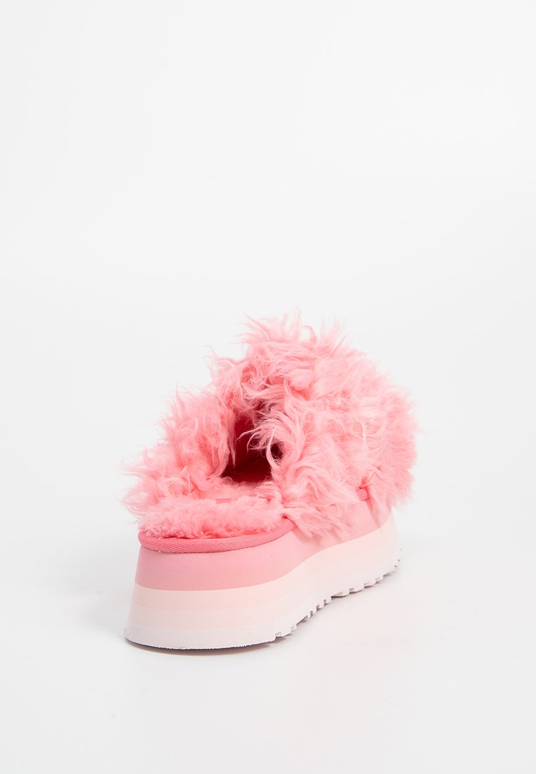 Scarpa con plateau rosa con suola spessa a strati bianca e rosa, coperta da morbido e riccio pelliccia sintetica, mostrata da una vista angolata posteriore su sfondo bianco.