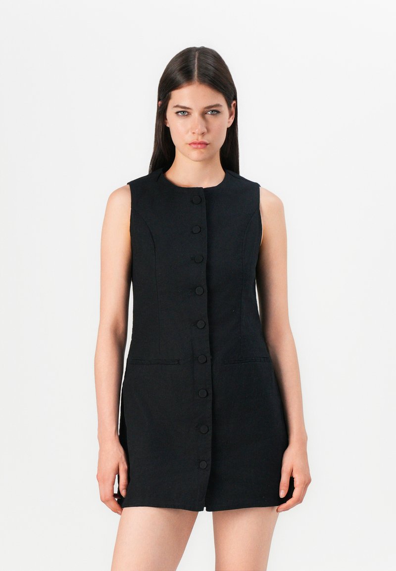 Robe noire sans manches avec une coupe droite, dotée d'un devant boutonné et de deux poches latérales. Fabriquée en tissu texturé.