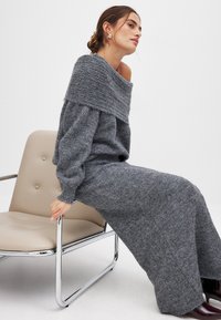 Gestricktes graues Zweiteiler-Outfit mit einem schulterfreien Pullover und einem langen Rock, der ein strukturiertes Muster und gerippte Bündchen aufweist.