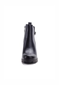 Bottine en cuir noir avec une finition lisse, bout arrondi et fermeture éclair sur le côté ; elle présente une semelle à crampons épaisse et une boucle en métal décorative.