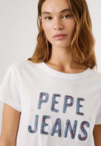 Bílý bavlněný tričko s výšivkou "PEPE JEANS" ve stylu modrého denimu a červenými akcenty; krátké rukávy a kulatý výstřih.