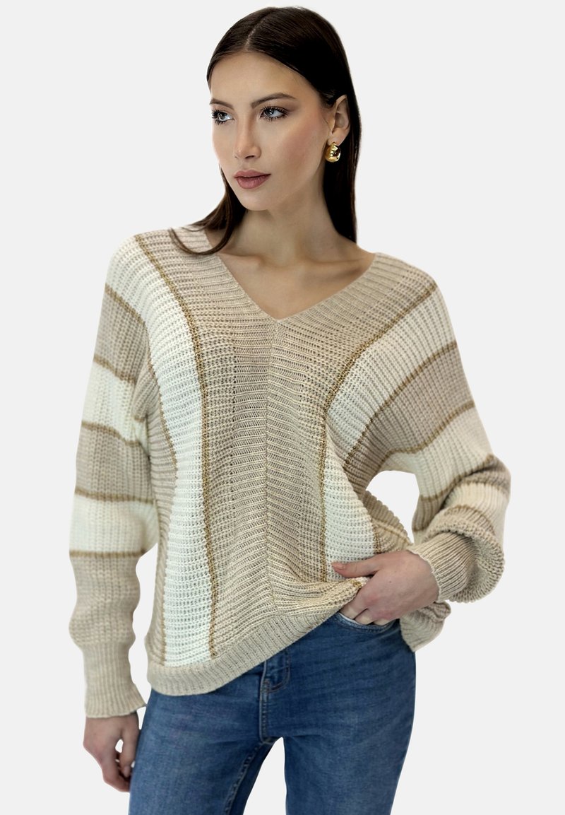 Jersey de punto beige y blanco con rayas horizontales, escote en V, mangas anchas y tejido texturizado. Combinado con vaqueros azules.