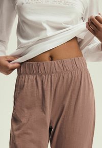 Bawełniana koszula z długim rękawem w jasnym kremowym kolorze, zestawiona z luźnymi spodniami w kolorze przykurzonego różu, posiadającymi elastyczny pas i miękką fakturę.