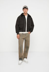 Crna bomber jakna s krznom oivičenim ovratnikom, dva prednja dzepa, uparen s svijetlosmešavim pantalonama i bijelim tenisicama, stvara ležeran izgled.