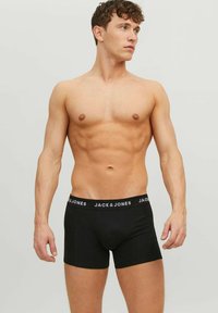 Shirtless man with a fit physique wearing black Jack & Jones boxer briefs, looking to the side against a plain light background.