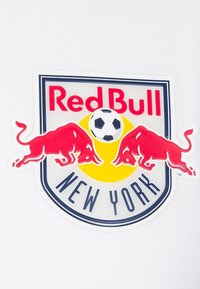 Logo Red Bull New York zobrazuje dva červené býky, žlutý kruh, fotbalový míč a text na bílém pozadí. Výrazný tvar štítu.