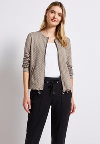 Vadderad, ljusgrå bomberjacka med rund halsringning, blixtlås fram och elastiska ärmslut; matchad med svarta byxor med dragsko i midjan.