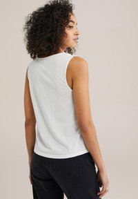 Fehér, ujjatlan felső, kerek nyakkivágással, puha, sima anyagból készült, fekete farmernadrággal párosítva. Egyszerű kialakítás, látható minták nélkül.