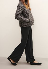 Schwarze Steppjacke mit strukturiertem Logo-Muster, kombiniert mit schwarzen, weiten Hosen und flachen schwarzen Schuhen. Einfache, legere Kleidung.