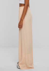 Licht perzikkleurige brede broek met een elastische tailleband, een soepele textuur en een vloeiende uitstraling, die perfect past bij een casual outfit.