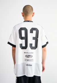Baltas tinklinis marškinėliai su juodais akcentais, didelis "93" nugaros pusėje ir "adidas" ženklas ant apykaklės bei kraštų.