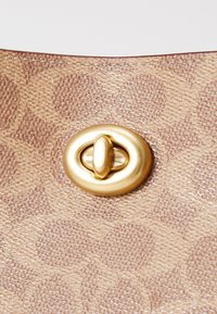 Tan leather handbag detail with a raised, textured pattern and a prominent gold-tone latch closure at the top.