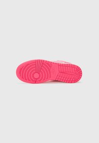Semelle de chaussure Nike rose vif avec des motifs de traction circulaires et en grille sur un fond gris clair uni.
