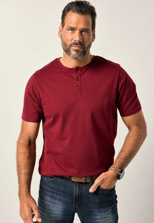 Maronenfarbendes Kurzarm-Henley-Shirt aus Baumwolle mit Knopfleiste, kombiniert mit dunkelblauen Jeans und einem braunen Gürtel.