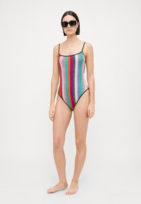 Maillot de bain une pièce avec des rayures verticales multicolores, fabriqué en tissu texturé, doté de fines bretelles noires et d'une coupe haute.