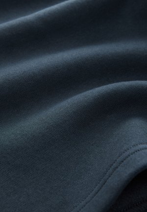 Ciemnogranatowa tkanina o gładkiej teksturze, z delikatnymi detalami szwów i łagodnymi fałdami, sugeruje miękki i przytulny materiał.