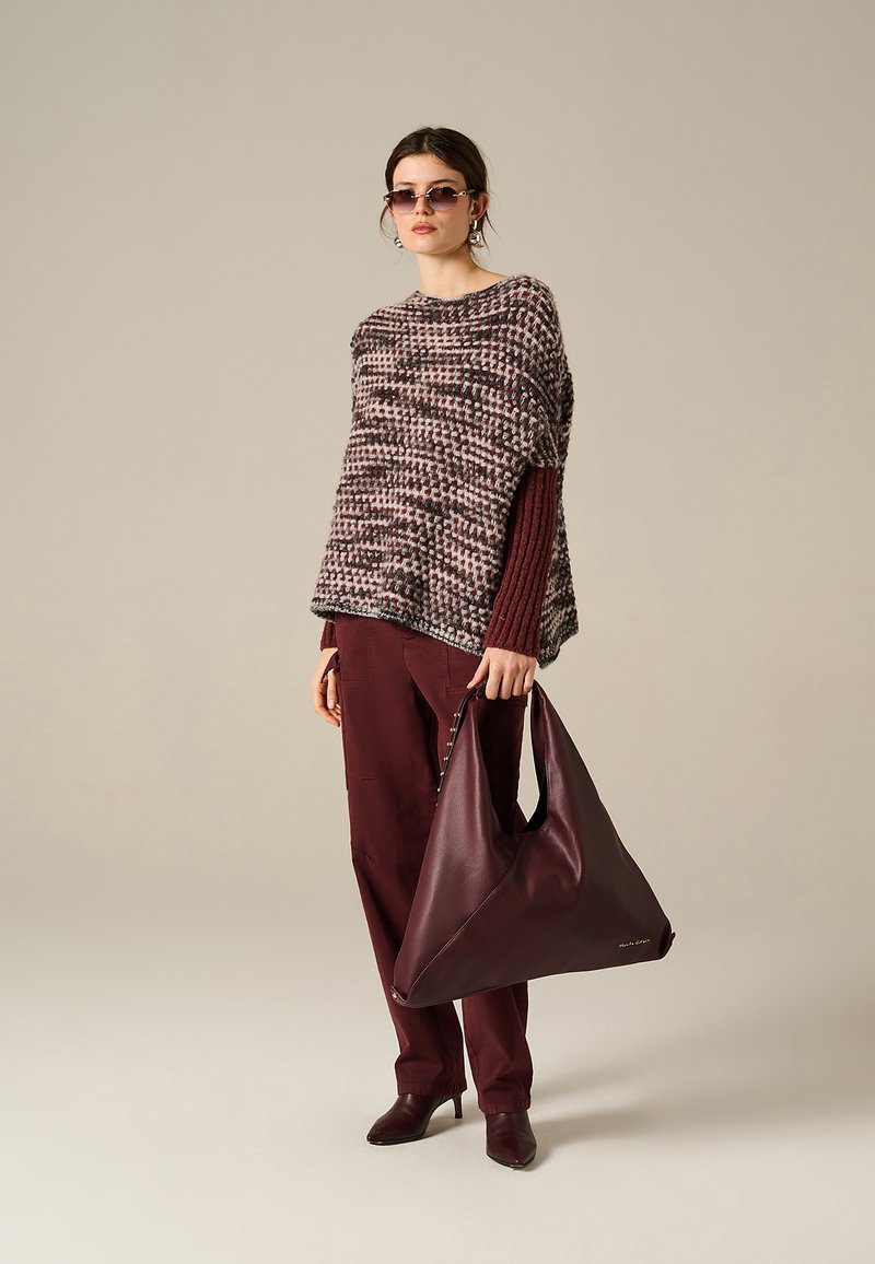 Poncho lavorato a maglia con motivi multicolore, abbinato a pantaloni borgogna e borsa coordinata. Il modello indossa occhiali da sole e stivali con tacco.