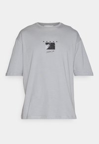 Camiseta de gran tamaño color gris claro con mangas cortas, que presenta un pequeño gráfico en blanco y negro y el texto "SENSE" y "Lossless Lab" en el pecho.