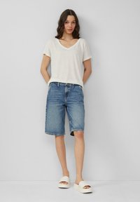 T-shirt blanc à col en V associé à un short en denim bleu marine. Le modèle porte des sandales à plateforme beige, avec une texture lisse et un design simple.