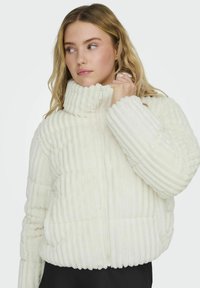 Giacca puffo bianca a coste con colletto alto e zip frontale. Tessuto morbido con strisce orizzontali distintive e polsini elasticizzati.