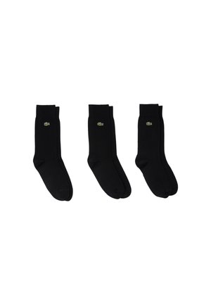 Calcetines negros con una textura suave y puños acanalados que presentan un pequeño logo verde de Lacoste en el lateral. Tres pares exhibidos en fila.