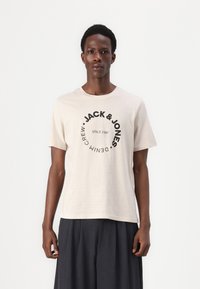 Beige cotton t-shirt with short sleeves, featuring a circular black graphic that includes "JACK & JONES" and "SINCE 1990" text.