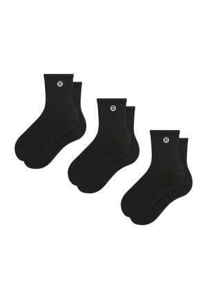 Tre par sorte ankelsokker med et hvidt rundt logo nær den øverste kant, vist på en hvid baggrund.