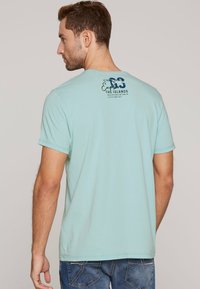 Jasnoniebieska koszulka z krótkim rękawem o okrągłym dekolcie z grafiką na plecach. Wykonana z bawełny, ma luźny krój i prosty design.