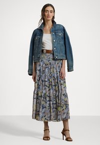 Jachetă din denim peste un top alb, cu o fustă maxi cu model floral albastru, având volane nivelate, și sandale cu toc maronii.