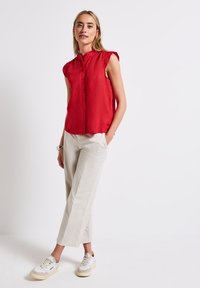 Camicia rossa senza maniche con colletto alto, abbinata a pantaloni larghi beige chiaro e sneakers bianche. Tessuto dalla texture morbida.