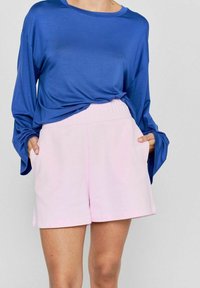 Royal blue langærmet top lavet af blødt stof, parret med lyserøde, mid-rise shorts med sidelommer og afslappet pasform.