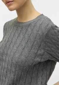Šedý pletený svetr s copánkovým vzorem, kulatým výstřihem a žebrovanými manžetami. Měkká textura je viditelná v detailu látky.