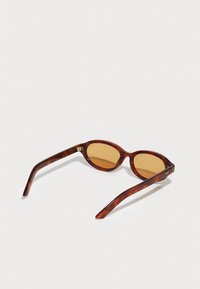 Ochelari de soare cu carapace de broască țestoasă maro, având lentile ovale, cu nuanțe portocalii și brațe subțiri și curbe. Branding-ul interior este vizibil pe ramele ochelarilor.