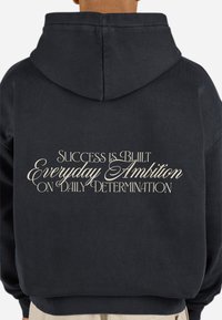 Black hoodie featuring a hood and ribbed cuffs. Text on the back reads “Success is Built Everyday Ambition on Daily Determination” in cream.