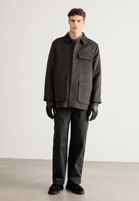 Σκούρο πράσινο μάλλινο παλτό με γιακά, εμπρόσθιες τσέπες, σετ με μαύρο παντελόνι και γάντια. Λείο υλικό με δομημένο σχεδιασμό.