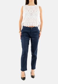 Top bianco senza maniche con design ad occhiello e orlo scallop, abbinato a pantaloni tapered blu navy e tacchi alti neri.