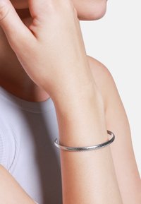 Pulsera de brazalete de plata con un patrón texturizado y trenzado. El diseño es elegante y minimalista, con una forma de extremo abierto.