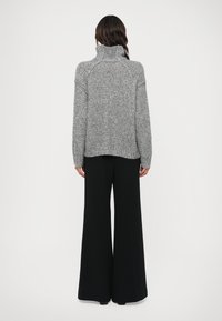 Suéter gris de punto con cuello alto y mangas caídas, combinado con pantalones negros de pierna ancha. La tela presenta un patrón texturizado y grueso.