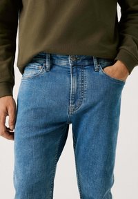 Blå denim jeans med en klassisk rett snitt, fem-lomme design og en subtil falmet tekstur. Brukt med en olivengrønn langermet skjorte.