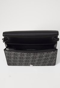 Černá kožená kabelka s texturovaným, vzorovaným povrchem. Má klopu na zavírání, kapsu na zip a uvnitř visačku s logem.