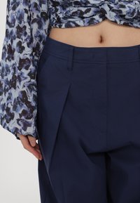 Navy pleated pants with side pockets, made from lightweight fabric. Worn with a floral patterned top featuring shades of blue and purple.